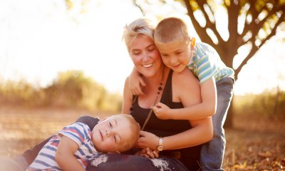 A mom and two young boys smiling and cuddling in a forest setting