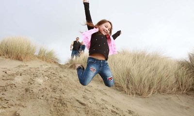 A happy young girl jumps onto beach from sand dune with arms outstretched 