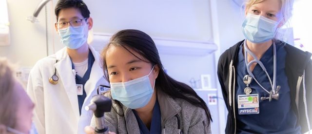 A provider oversees a resident caring for a patient in a clinical setting.