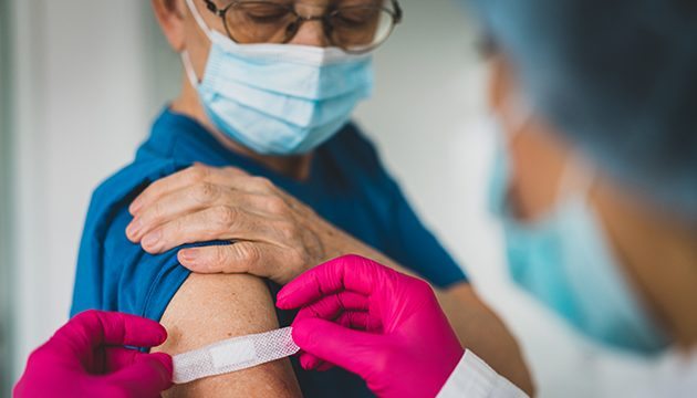 A masked patient is bandaged by a healthcare provider after a vaccination.