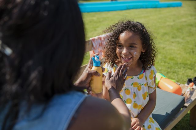 Woman applying sunscreen to a kid's face.