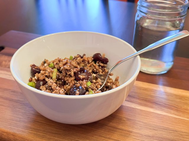 Cherry, quinoa and wild rice salad in white bowl with a glass of water.