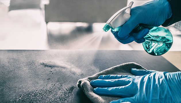 Gloved hands spray and wipe a surface