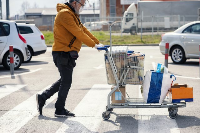 Person wearing a mask and gloves pushes a full grocery cart