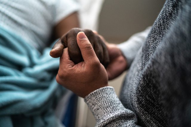 A father holds the hand of his son in a comforting manner.