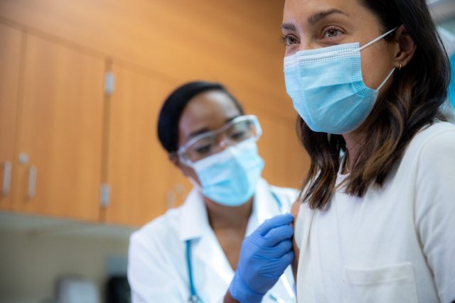 A young woman gets a flu shot in her right shoulder.