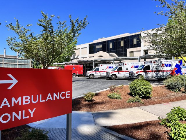 Emergency room parking lot with "Ambulance Only"  sign in the foreground and a row of ambulances in the background