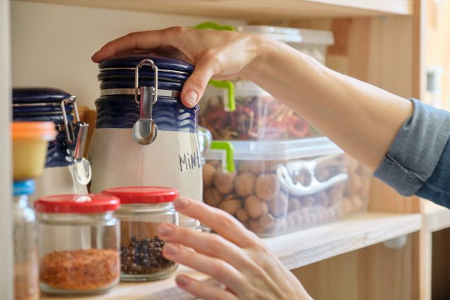 Hands of a woman reaches for a jar in a pantry shelf of dry foods