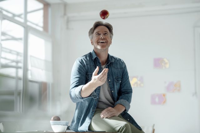 Man sits on table and catches an apple