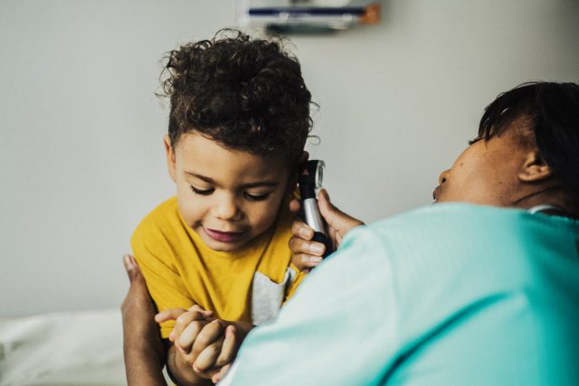 Caregiver taking child's temperature with ear thermometer.