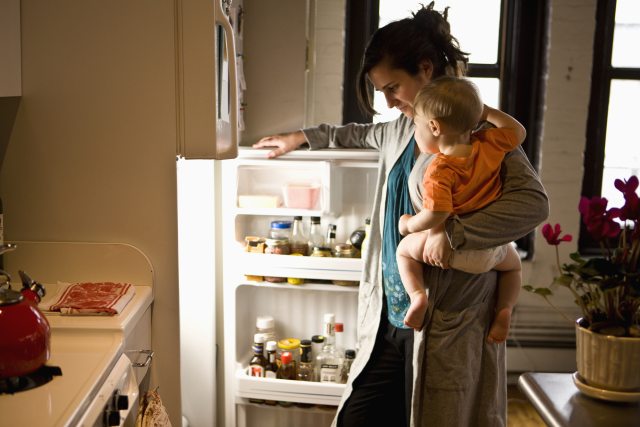 Woman looking in fridge with child on hip.