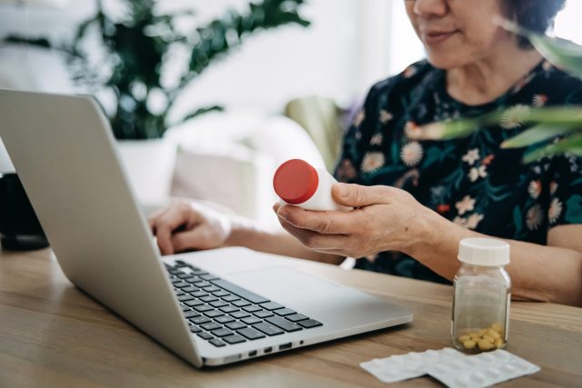 Woman checks medicine bottle as she works on laptop