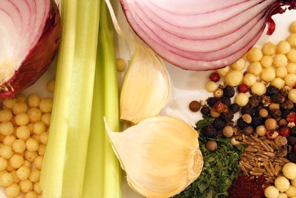 Closeup of garlic, onion slices, celery stalk, peppercorns and other spices
