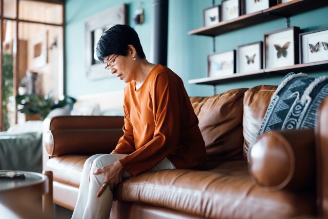 Woman sitting on a brown couch rubs her knee