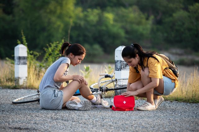 Young woman gives first aid to another woman sitting next to bicycle