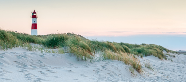 A sandy beach with grassy embankment and red and white lighthouse in the background