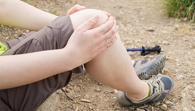 Closeup of hands of hiker holding painful knee