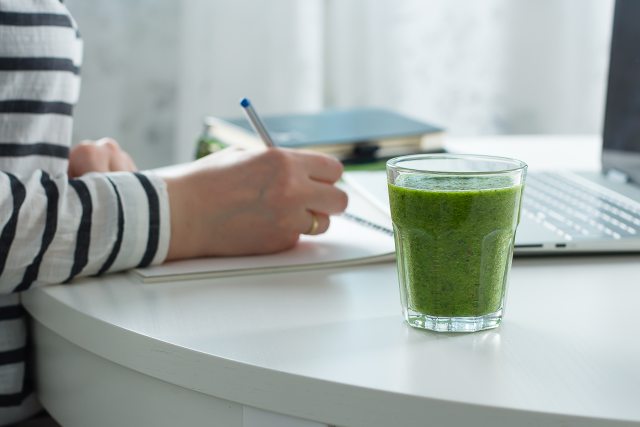 Woman working on computer with green drink next to her.