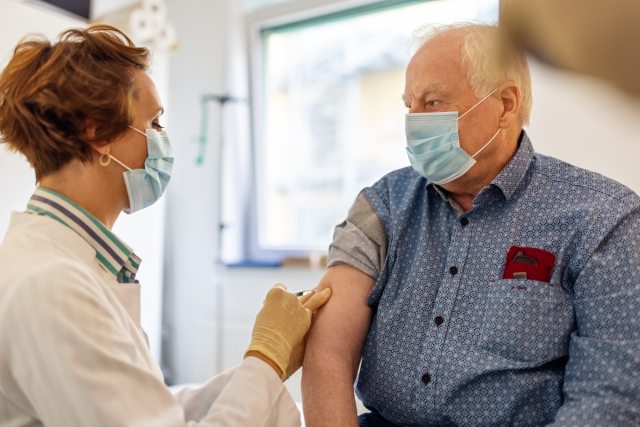 Woman healthcare provider gives immunization in arm of grey-haired man
