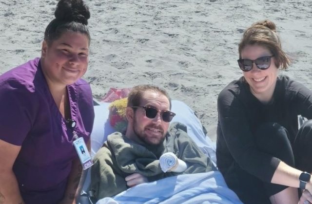 Aidan, Aidan's sister and caregiver Sandra Farris posing on the beach.