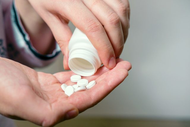 Closeup of person's hands pouring white pills from bottle