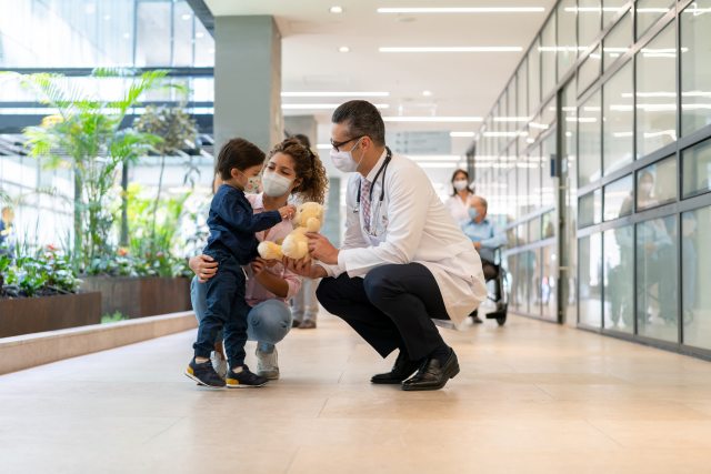 A young child and mother squat next to a doctor in a healthcare facility