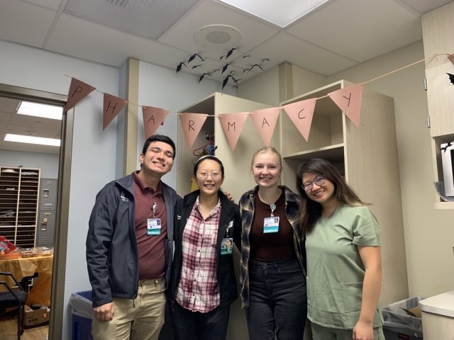 4 residents from 2023-24 gather and pose for the camera in a room with the letters P-H-A-R-M-A-C-Y spelled out above them