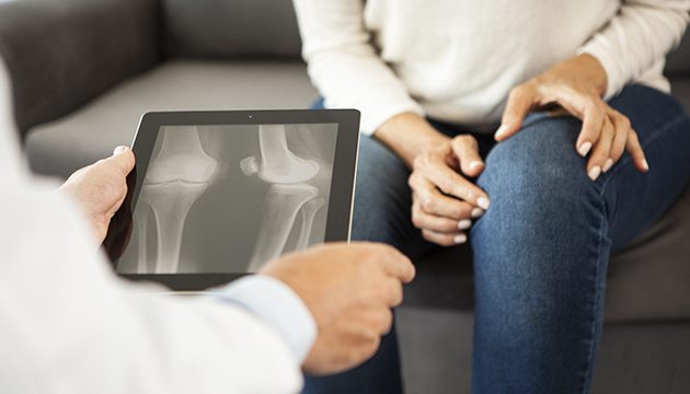 Closeup of doctor's hands holding X-ray and woman pointing to knee