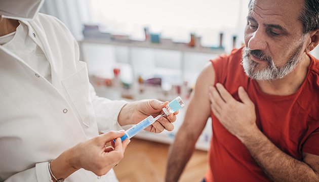 Pharmacy technician prepares to give vaccination to bearded man