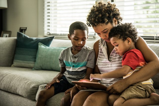 A woman sits on the couch with two children, working a tablet