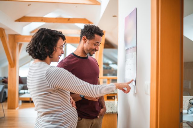Pregnant woman and partner look together at a wall calendar