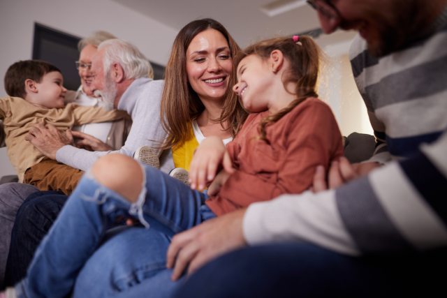 Family with two children, a parent and a grandparent laughing and smiling while sitting on a couch in the living room