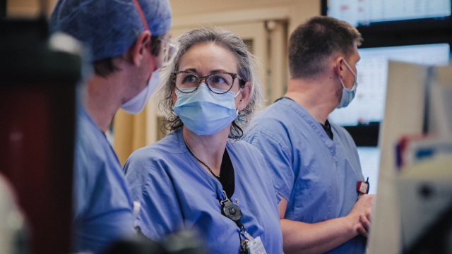 Three healthcare providers wearing blue scrubs and face masks.