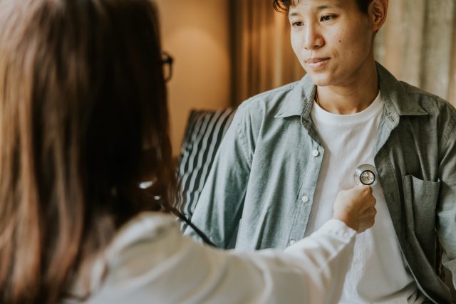 Transgender man meeting with  female doctor who is using a stethoscope on the patient's chest area.