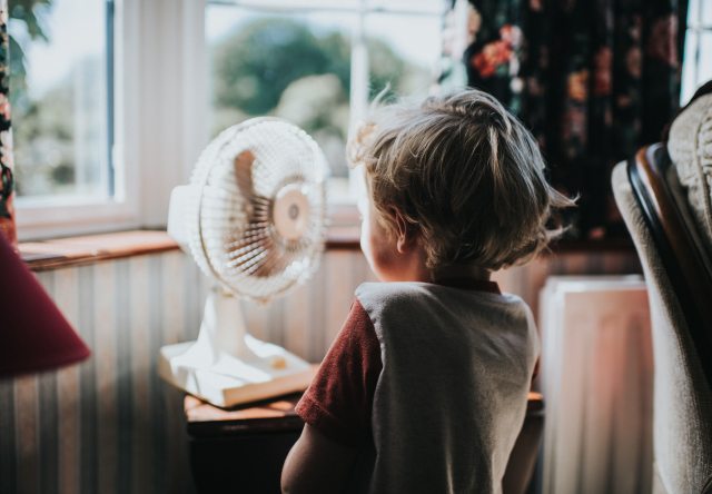 Young child stands in front of a cooling fan indoors