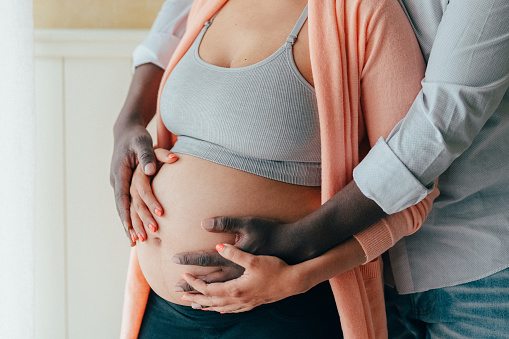 Expectant couple clasping hands across the pregnant partner's growing belly