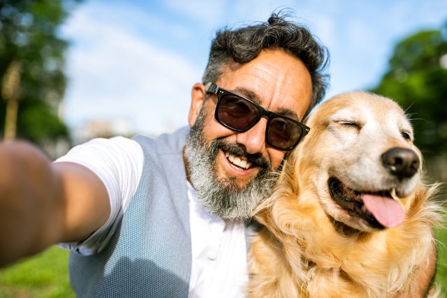 Man wearing sunglasses taking a selfie with his golden retriever.