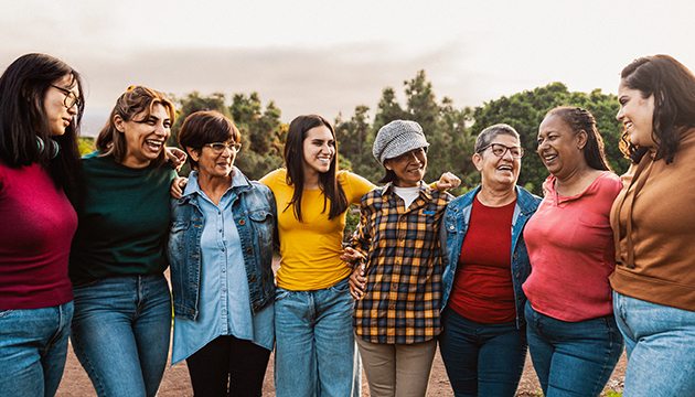 A group of 8 smiling women of various ages in an outdoor setting