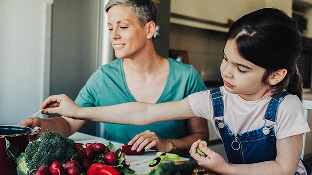 An adult woman and youjng girl sort through vegetables laid out on the kitchen counter