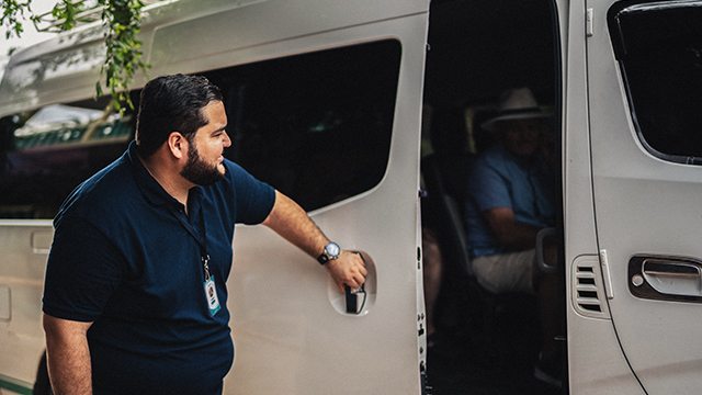 An adult male opens the door of a large van transporting senior citizens