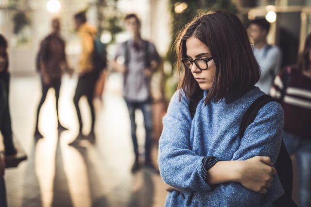 Worried teenage girl wearing backpack at school.