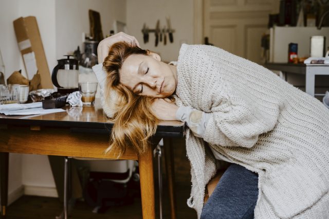 Sleepy woman with long blond hair slumps over a kitchen table