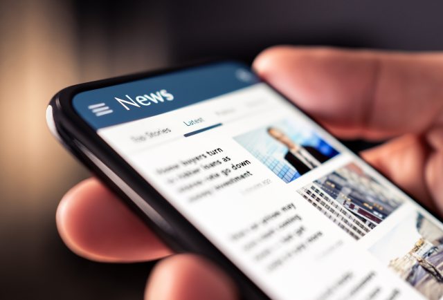 Closeup of hand holding a cell phone with news on the screen