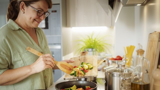 Smiling older woman stirs veggies in a pan on the stove