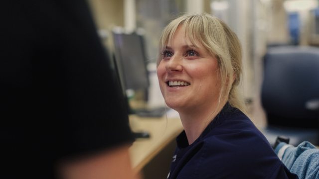 A female nuse smiles at another nurse while seated at a workstation