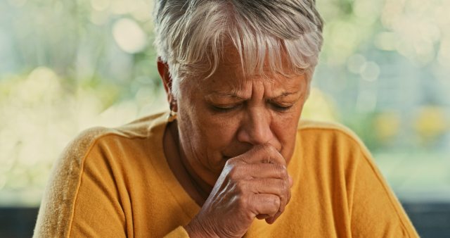 Woman with short silver hair coughs into her hand