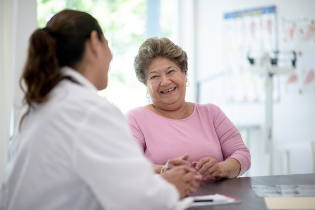 Smiling woman with short salt-&-pepper hair sits and talks with a doctor in a white coat