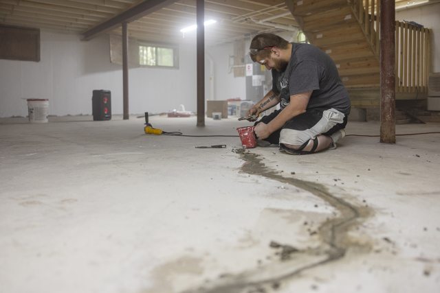 Kneeling man works to seal cracks in floor of basement