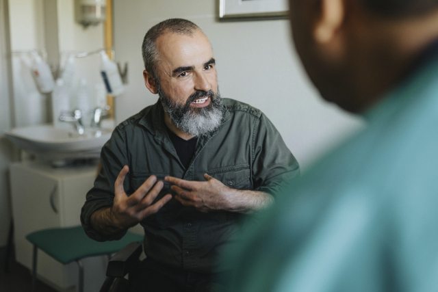 Bearded man talks expressively with a provider in an exam room
