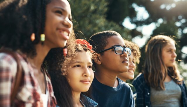 A group of kids look at something off camera, several smiling, several more serious
